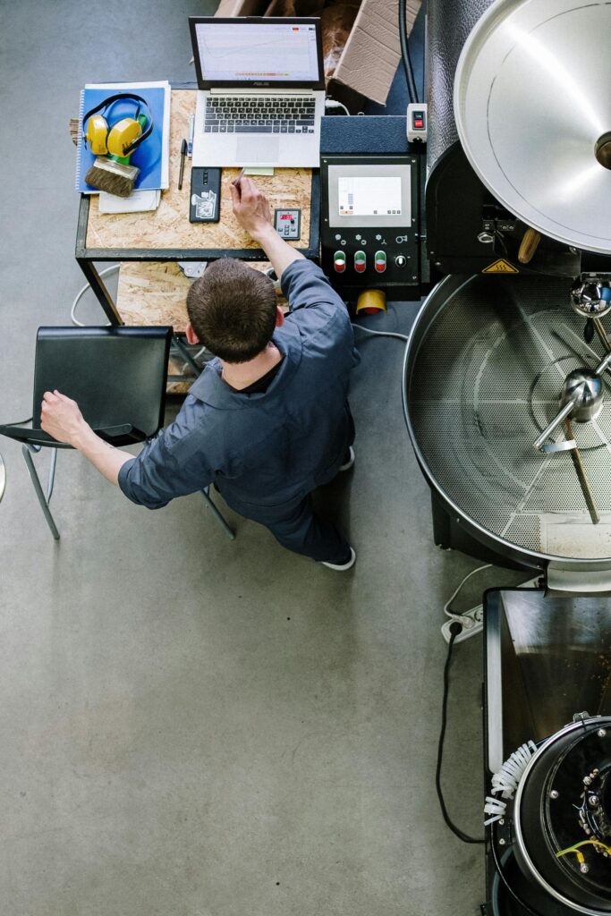 Overhead view of technician operating coffee roasting equipment in an industrial setting.