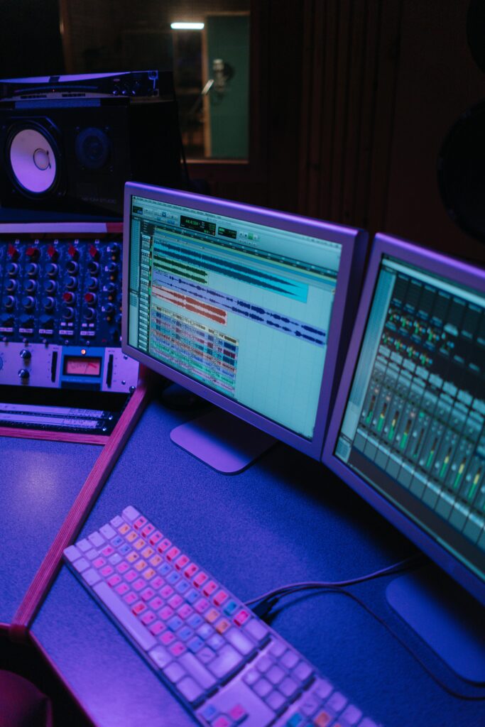 A vibrant music studio featuring mixing consoles and computer screens under neon light.