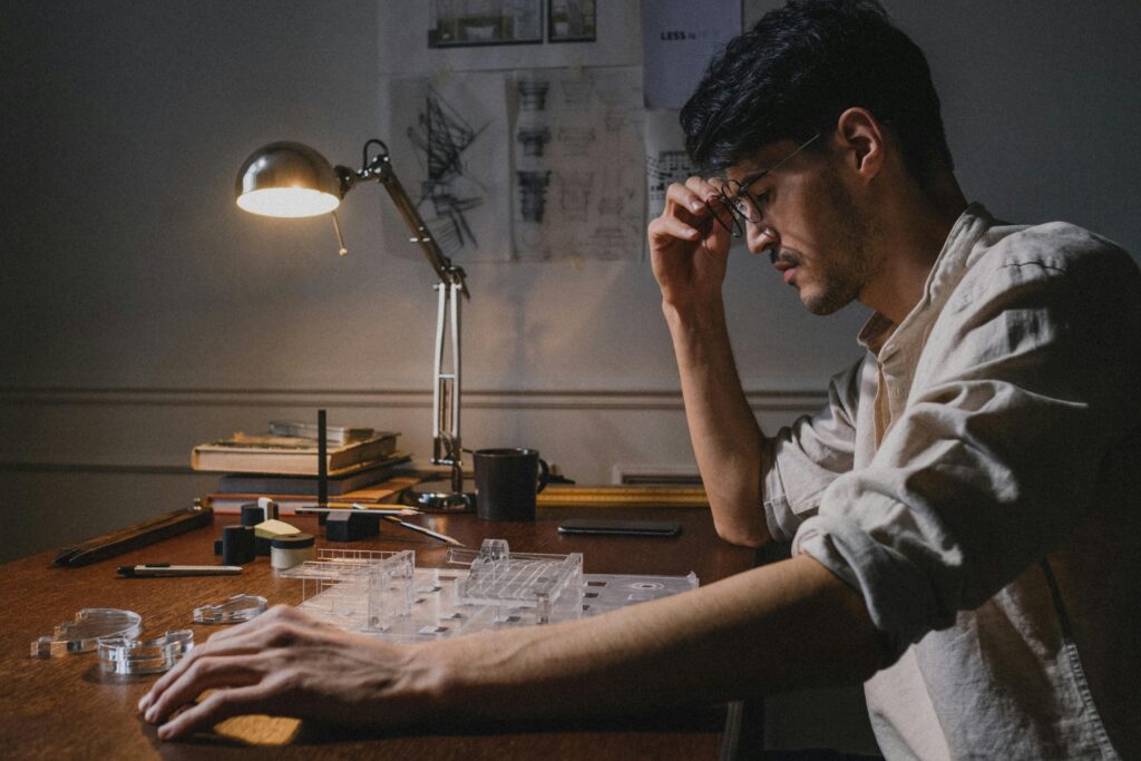 Architect seated at a desk, working on a model under a desk lamp, focusing intently.